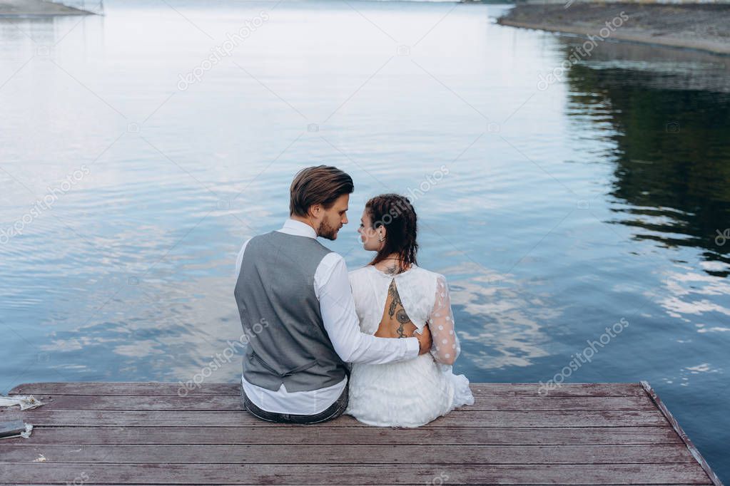 back view beautiful couple sitting on a wooden pier against lake