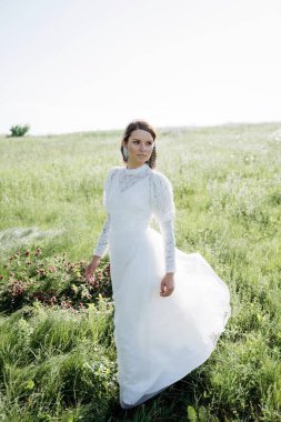 Beyaz elbiseli genç bir kadın yaz çayırında dikiliyor. 