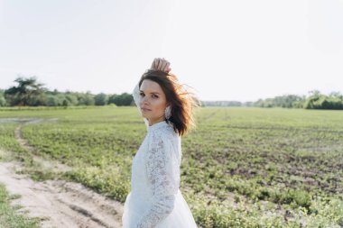 Beyaz elbiseli şık bir kadın tarlada ayakta duruyor.