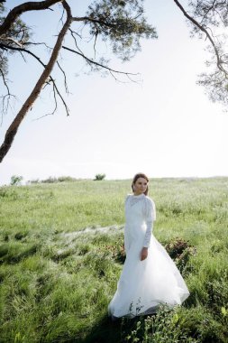 Beyaz elbiseli genç bir kadın yaz çayırında dikiliyor. 
