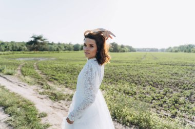 Yeşil tarlada duran uzun beyaz elbiseli çekici kadının portresi. 