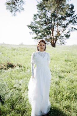 Beyaz elbiseli genç bir kadın yaz çayırında dikiliyor. 