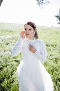 Yeşil tarlada duran uzun beyaz elbiseli çekici kadının portresi. 