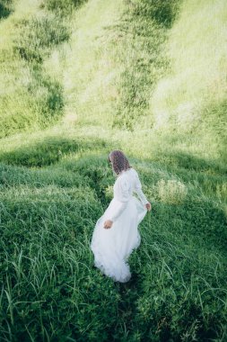 Yeşil dağ bölgesinde duran beyaz elbiseli şık bir kadının arka manzarası. 