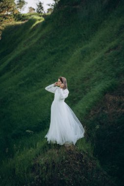 Yeşil dağ manzarasında duran beyaz elbiseli şık bir kadın.