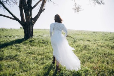 Tarlada yürüyen uzun beyaz elbiseli şık bir kadının arka plan görüntüsü. 