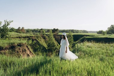 Beyaz elbiseli gelin yeşil alanda duruyor.