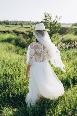 Beyaz elbiseli fötr şapkalı şık bir kadın tarlada dikiliyor. 