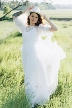Çayırda duran fötr şapkalı, beyaz elbiseli neşeli kadın.