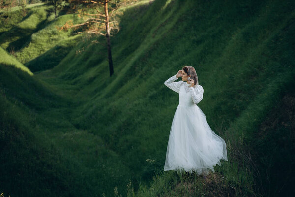 Fashionable woman in white dress standing in the green mountain landscape