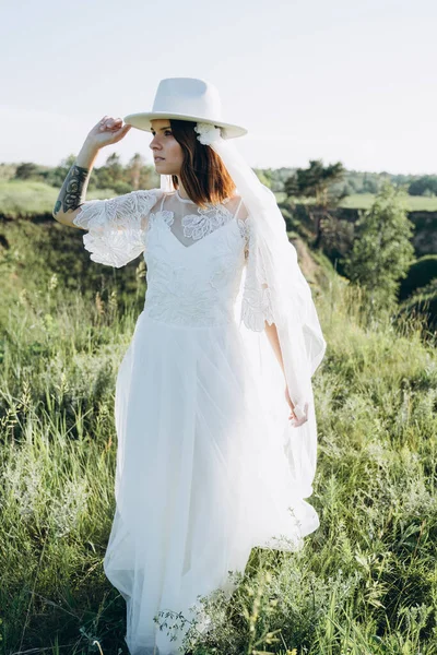 pretty woman in stylish fedora hat standing in green area