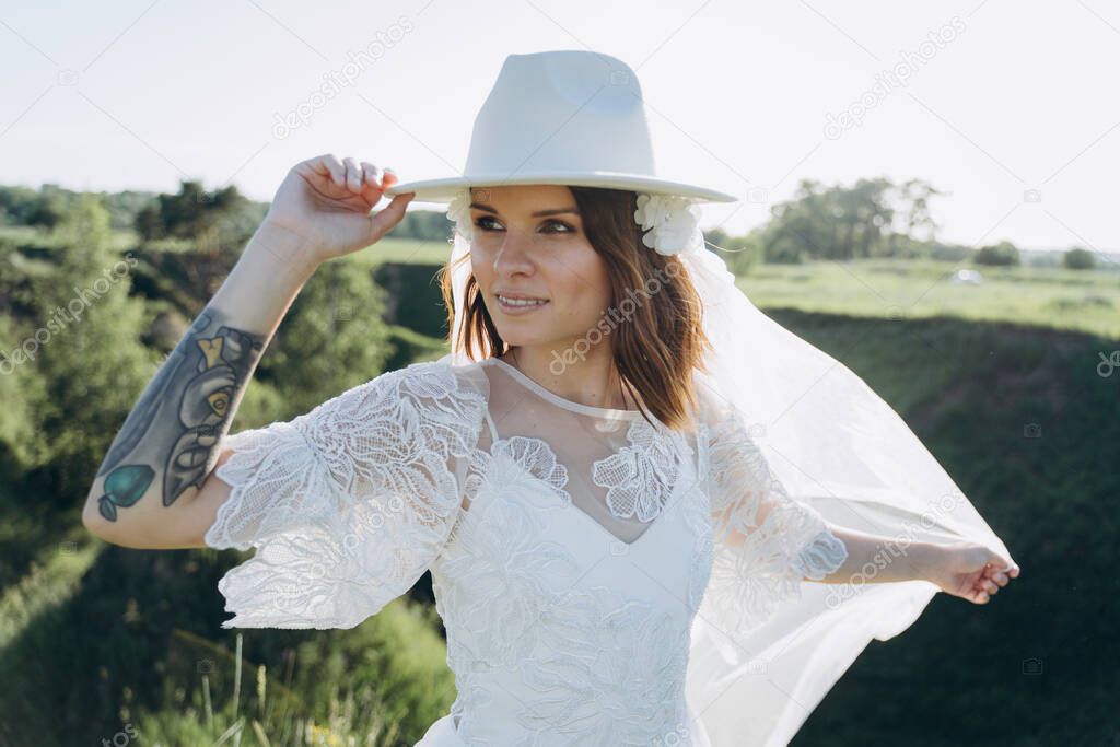 pretty young woman wearing fedora hat and and long white dress standing  in the meadow