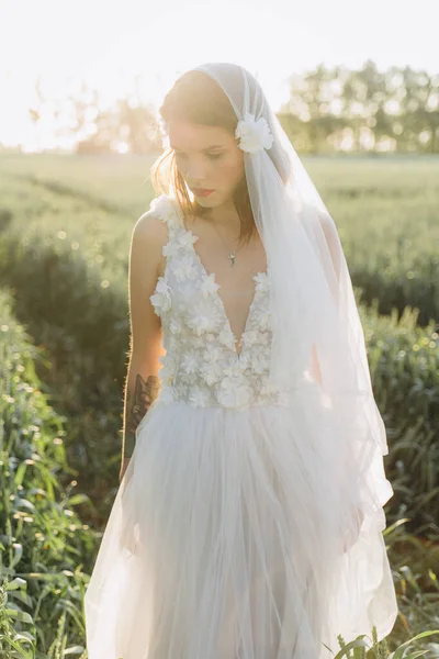 young woman wearing veil and long white dress standing in the meadow