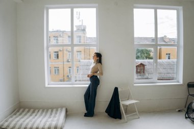 Odada pencerede duran kotlu şık bir kadın.