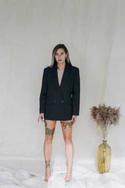 Siyah ceketli dövmeli kız kameraya bakıyor.