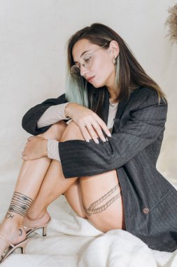 Stüdyoda kumaş üzerinde oturan şık dövmeli kız.