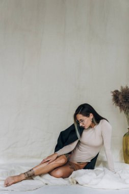 Ceketli, dövmeli kadın kumaşın üzerinde oturuyor.