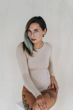 Genç bayan sandalyede oturuyor ve stüdyoda kameraya gülümsüyor.