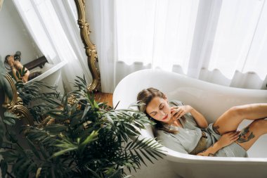 Genç bayan boş bir küvette yatıyor, tepeden bakıyor. 