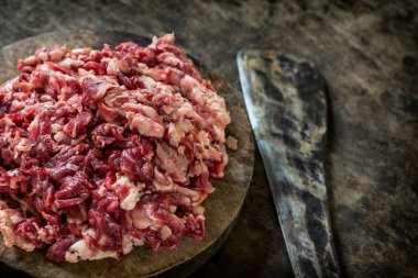 Parçalanmış ham sığır eti kesme tahtası üzerinde bıçak ile.