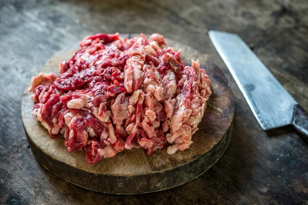 Parçalanmış ham sığır eti kesme tahtası üzerinde bıçak ile.