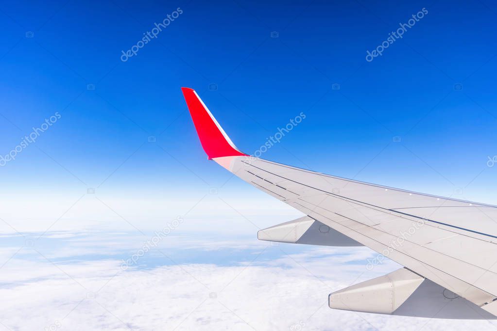 View from window of aircraft left wing on the blue sky above the clouds.