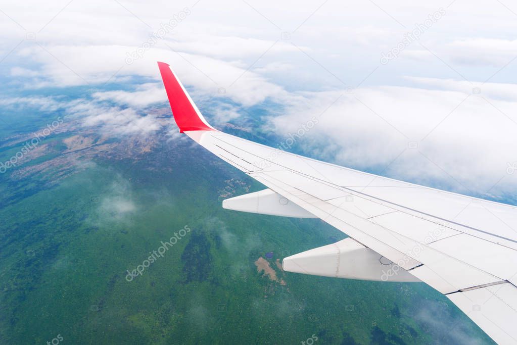 View from window of airplane wing in the clouds, looking down the green ground.