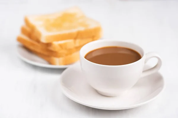 Cup of coffee and sliced bread on white table, breakfast