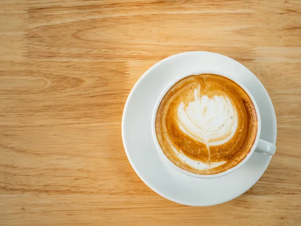 Bir fincan latte sanat kahvesi, ahşap masa, üst manzara.