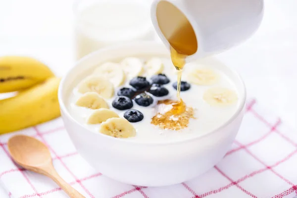 Verter miel sobre harina de avena con plátano y arándanos —  Fotos de Stock