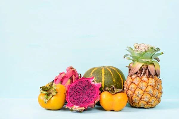 Tropical fruits (persimmon, dragon fruit, pineapple and melon) on pastel background
