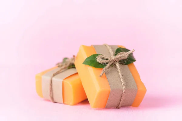Orange soap wrapping with paper and ribbon on pink background, herbal homemade soap
