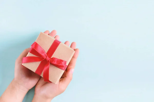 Manos Sosteniendo Caja Regalo Con Cinta Roja Sobre Fondo Pastel — Foto de Stock