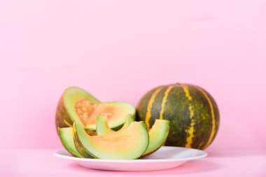 Beyaz tabakta dilimlenmiş kavun ve pembe pastel arka plan.