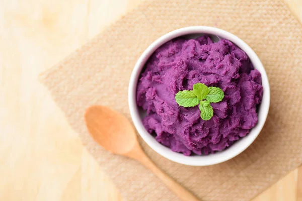 Mashed purple sweet potatoes in a bowl with spoon on wooden table, Healthy food