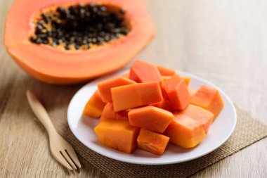 Dilimlenmiş papaya meyvesi beyaz tabakta çatalla ahşap masada yemeye hazır, tropik meyve