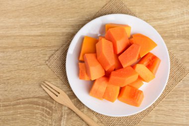 Dilimlenmiş papaya meyvesi beyaz tabakta çatalla ahşap arka planda yemeye hazır tropikal meyve, üst manzara