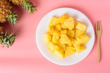 Beyaz tabakta dilimlenmiş ananas meyvesi. Çatalla birlikte pastel pembe arka planda yemeye hazır. Tropik meyve.