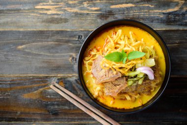 Kuzey Tayland yemeği (Khao Soi), baharatlı körili şehriye çorbası ve kıtır kıtır kızarmış yumurtalı şehriye, turşulu hardal, arpacık soğanı ve ahşap zemin üzerinde limon.