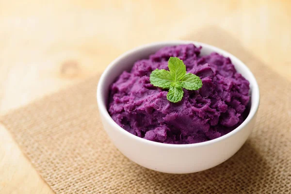Mashed purple sweet potatoes in a bowl on wooden table, Healthy food