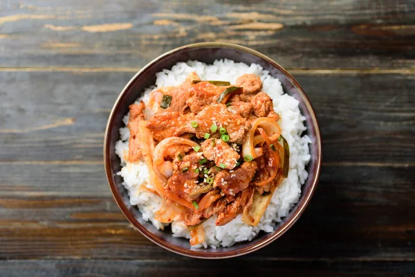Stir fried kimchi with pork on cooked rice in a bowl on wooden background, Korean food