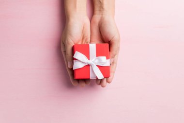 Pembe arka planda beyaz kurdeleli kırmızı hediye kutusu, özel bir gün için hediye, Top view