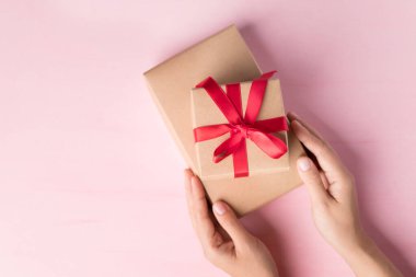 Pembe arka planda kırmızı kurdeleli kağıt hediye kutusu, özel bir gün için hediye, Top view