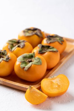 Tahta tabakta taze olgun hurma, beyaz arka plan, sonbahar tatlı meyvesi