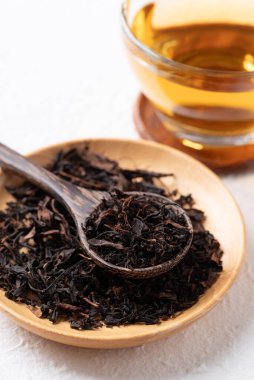 Tahta kasede kurumuş siyah çay yaprakları kaşık ve bardakta sıcak çay, sağlıklı bitkisel içecekler.