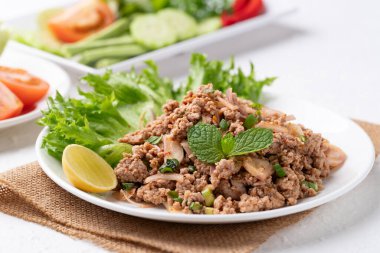 Yerel Tayland yemekleri, baharatlı domuz salatası (Larb Moo) beyaz arka planda taze sebzelerle yemek