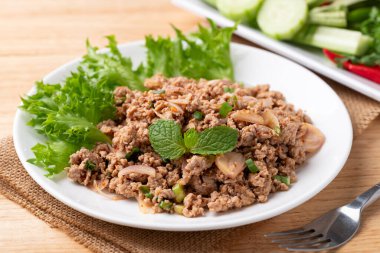 Yerel Tayland yemeği, baharatlı domuz salatası (Larb Moo) ve ahşap arka planda taze sebze yemek.