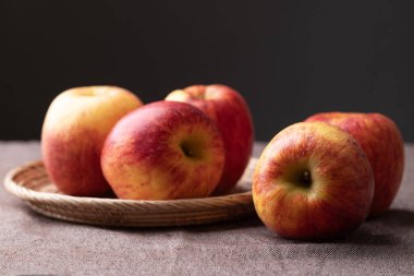 Siyah arkaplanlı kahverengi kumaş üzerinde kırmızı elma (Envy apple) sepeti