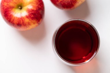 Beyaz arka planda kırmızı elma meyveli bir bardak elma şarabı.