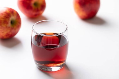 Beyaz arka planda kırmızı elma meyveli bir bardak elma şarabı.